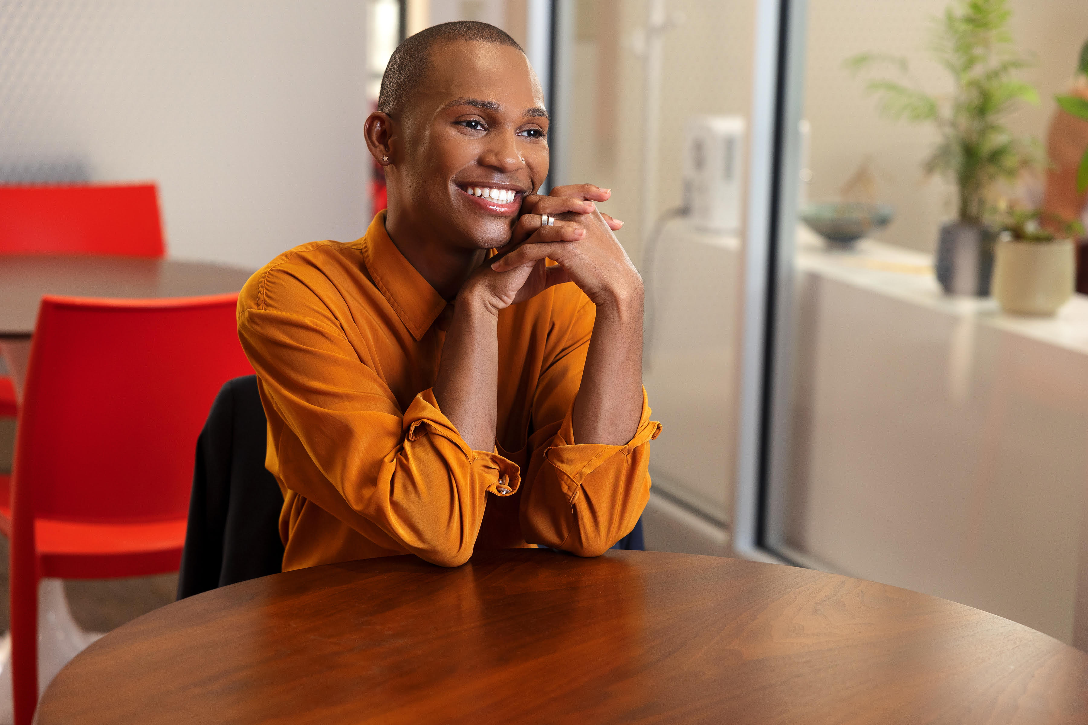 Dae Williams smiling at a table in an orange shirt